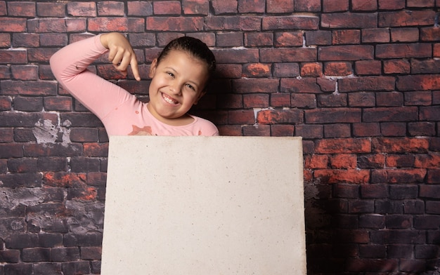 Piccola ragazza che fa pose con lettere di carta riciclata vuote davanti a un vecchio sfondo di muro di mattoni, sfondo scuro, messa a fuoco selettiva.