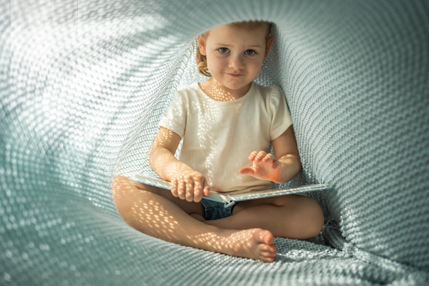 Piccola ragazza che si diverte a recensire un libro sotto un vestito a quadri a maglia blu in una mattinata soleggiata