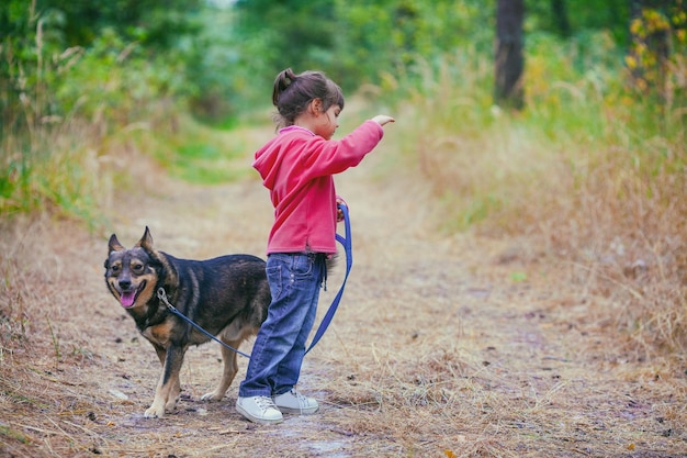 Piccola ragazza con un cane che cammina nella foresta