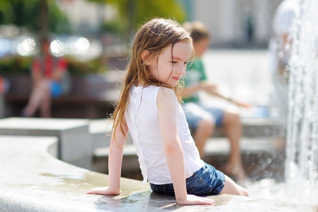 Piccola ragazza del bambino in età prescolare che gioca con una fontana della città il giorno di estate