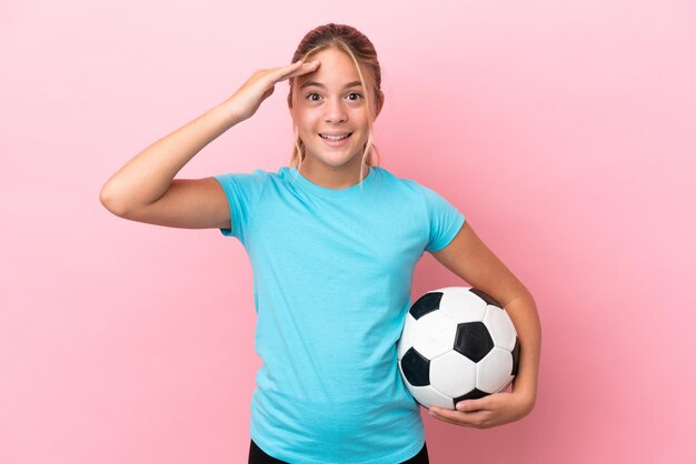 Piccola ragazza del giocatore di football isolata su fondo rosa con l'espressione di sorpresa