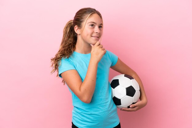 Piccola ragazza del giocatore di football isolata su sfondo rosa che guarda di lato e sorride