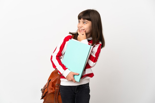 Piccola ragazza dell'allievo isolata su priorità bassa bianca che osserva al lato e sorridente