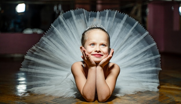 Piccola ragazza della ballerina in un tutù bianco. Adorabile bambino posa sul pavimento in uno studio.