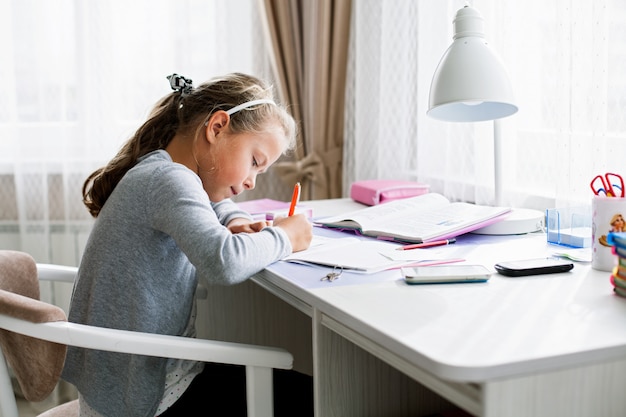 Piccola ragazza della scuola che scrive qualcosa in un quaderno