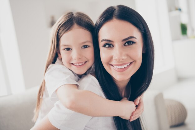 Piccola ragazza e giovane mamma che abbraccia piggyback in casa casa al chiuso