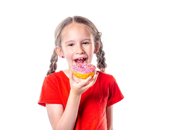 Piccola ragazza europea sveglia con le trecce che mangia la ciambella isolata su fondo bianco.