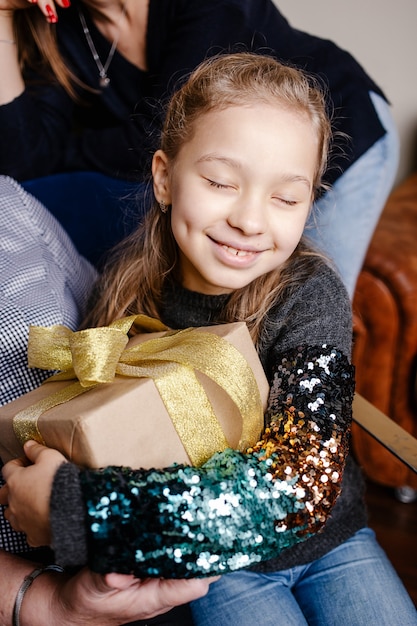 Piccola ragazza felice sveglia che abbraccia il suo regalo di Natale. Bambino entusiasta di disimballare il suo regalo