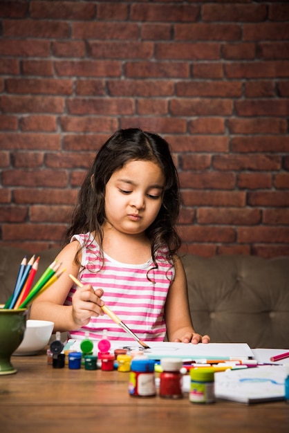 Piccola ragazza indiana che disegna o dipinge con i colori su carta, messa a fuoco selettiva