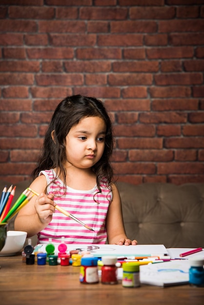 Piccola ragazza indiana che disegna o dipinge con i colori su carta, messa a fuoco selettiva