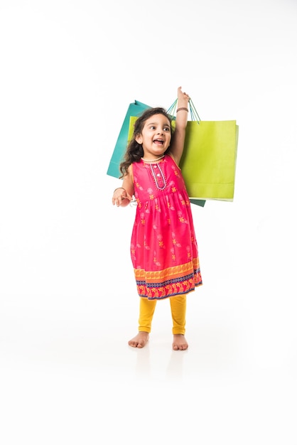 Piccola ragazza indiana che tiene le borse della spesa, in piedi isolato su sfondo bianco