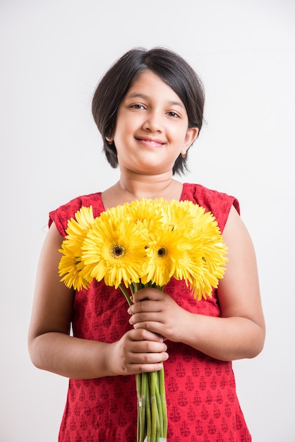 Piccola ragazza indiana sveglia che tiene un mazzo o un mazzo dei fiori gialli freschi della gerbera. Isolato su sfondo bianco