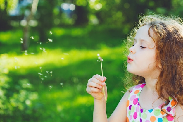 Piccola ragazza riccia che soffia il dente di leone.