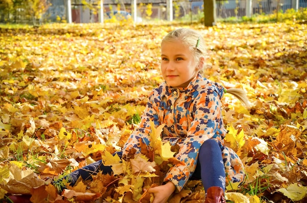 Piccola ragazza seduta in foglie d'acero e sorridente