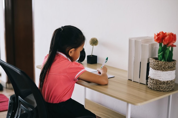 Piccola ragazza si siede al tavolo scrive nel quaderno di esercizi prepara i compiti per la scuola