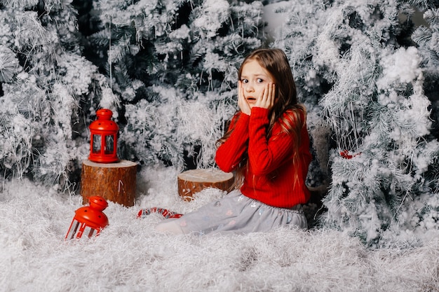 Piccola ragazza sorpresa che si siede vicino all'albero di Natale