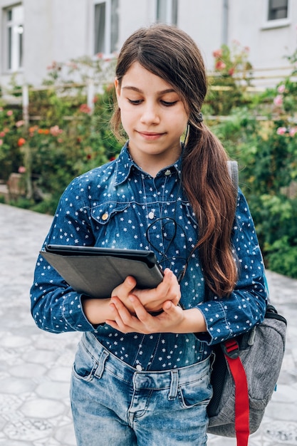 Piccola ragazza sorridente della scolara con il computer portatile in mano, torna a scuola e il concetto di carriera femminile di successo