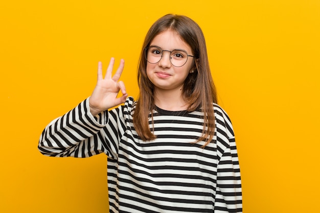 Piccola ragazza sveglia caucasica allegra e sicura che mostra gesto giusto.