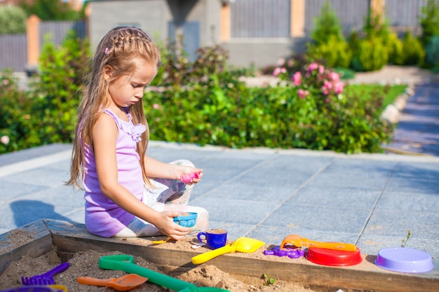 Piccola ragazza sveglia che gioca al sandbox con i giocattoli nell'iarda