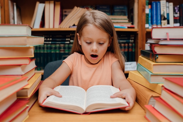 Piccola ragazza sveglia che legge nella biblioteca