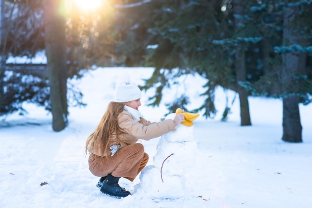 Piccola ragazza sveglia che si diverte a giocare a fare il pupazzo di neve nella foresta invernale innevata