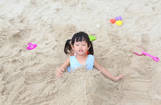 Piccola ragazza sveglia del bambino asiatico che gioca sabbia alla spiaggia