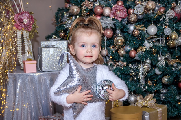 Piccola ragazza sveglia vicino all'albero di Natale. Capodanno e Natale. Decorazione dell'albero di Natale.