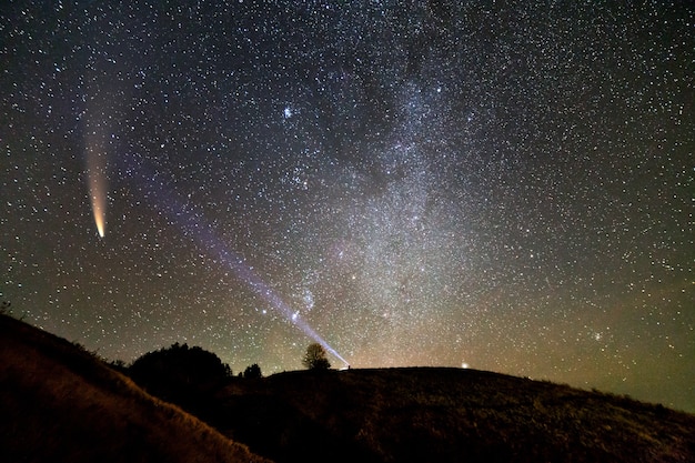 piccola sagoma di uno scienziato con una torcia in testa che punta un raggio di luce brillante sul cielo