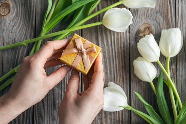 Piccola scatola regalo in mani femminili su uno sfondo di legno con tulipani vista dall'alto