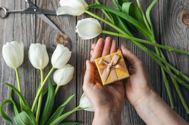 Piccola scatola regalo in mani femminili su uno sfondo di legno con tulipani vista dall'alto