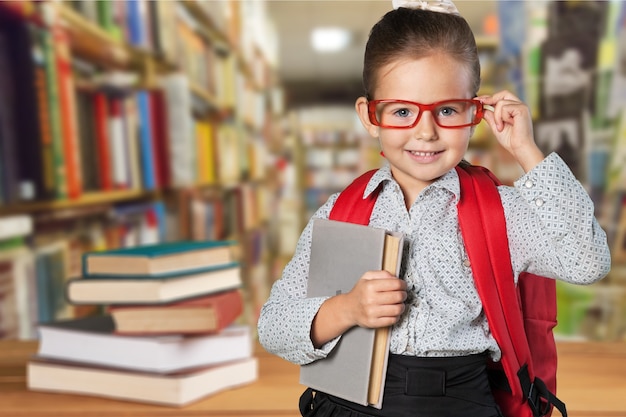 Piccola studentessa carina con gli occhiali con libri sullo sfondo