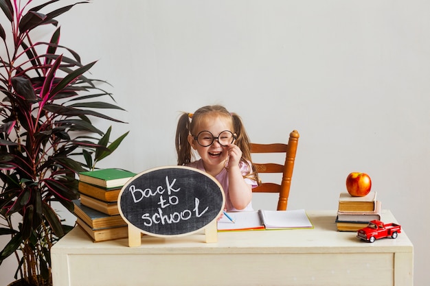 Piccola studentessa carina con gli occhiali si siede alla sua scrivania a scuola con i libri di testo