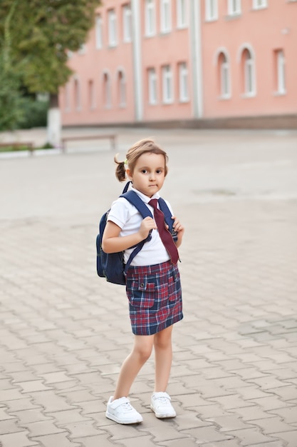 Piccola studentessa carina in uniforme con zaino da scuola