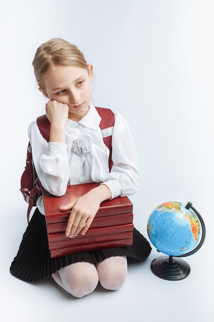 Piccola studentessa carina ragazza seduta con libri e un globo, sorridente e felice