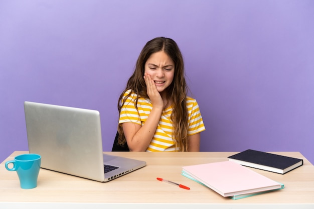 Piccola studentessa in un posto di lavoro con un computer portatile isolato su sfondo viola con mal di denti