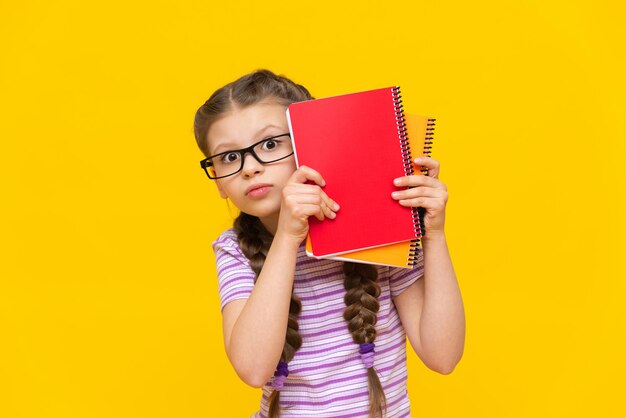 Piccola studentessa sorpresa su uno sfondo isolato Una ragazza con libri di testo e quaderni con gli occhiali