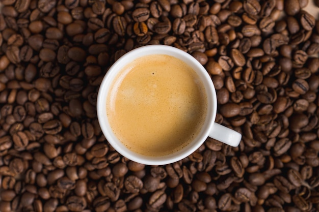 Piccola tazza di caffè bianco con crema espresso su sfondo di chicchi tostati Messa a fuoco selettiva Vista dall'alto