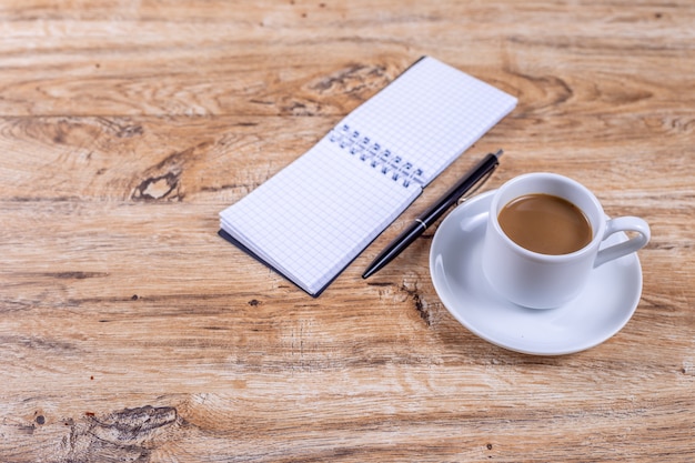 Piccola tazza di caffè bianco su un piattino accanto a un taccuino e una penna