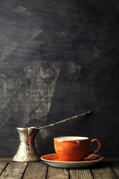 Piccola tazza di caffè in ceramica e vecchia caffettiera sul nero con spazio di copia.