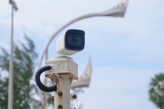 Piccola telecamera CCTV su strada bianca su un palo arrugginito lungo la strada