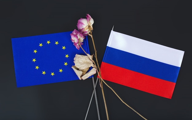 Piccole bandiere dell'Unione Europea e della Federazione Russa e due fiori secchi su una superficie nera. sfondo