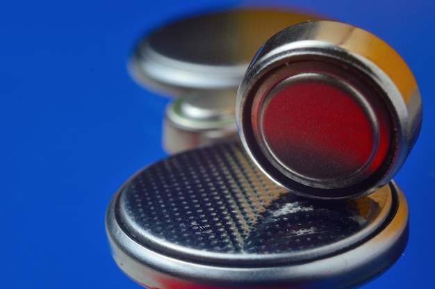 Piccole batterie a bottone di diverse dimensioni, evidenziate in rosso e arancione, giacciono su uno sfondo blu. avvicinamento.