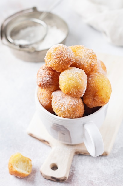 Piccole ciambelle. Biscotti di ricotta fatti in casa fritti e cosparsi di zucchero a velo in una tazza di ceramica vintage su sfondo chiaro. Messa a fuoco selettiva.