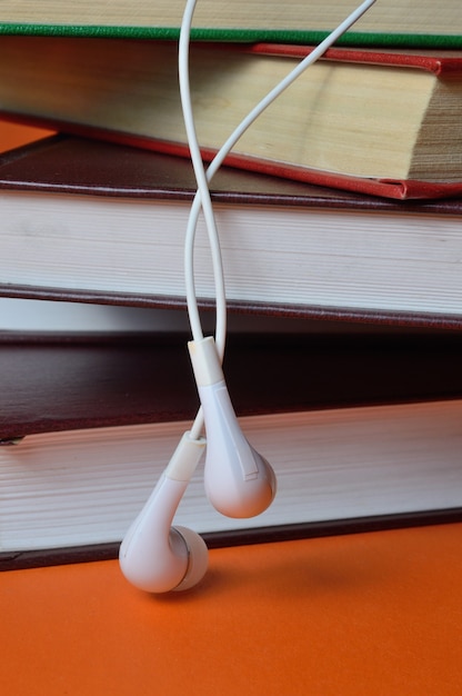 Piccole cuffie bianche dal telefono giacciono su una pila di libri su uno sfondo arancione.