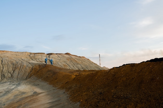 Piccole figure di due ricercatori contemporanei in conall protettivi che si muovono lungo la collina durante l'indagine scientifica dell'area abbandonata