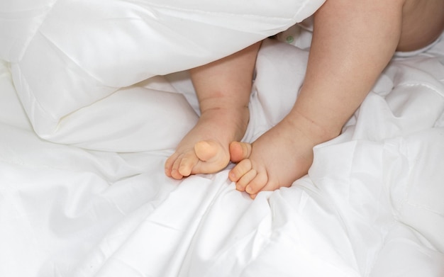 Piccole gambe del bambino sotto la coperta bianca