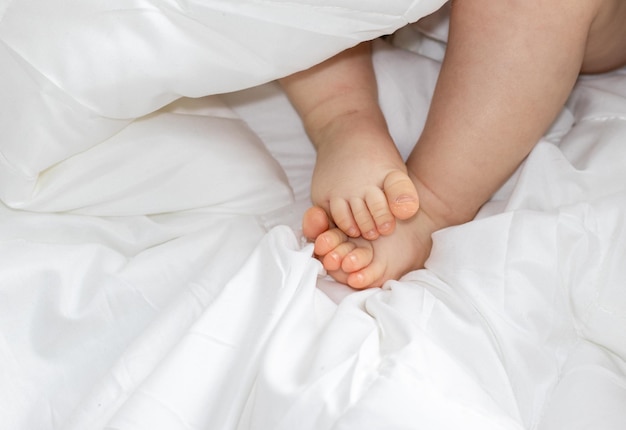 Piccole gambe del bambino sotto la coperta bianca