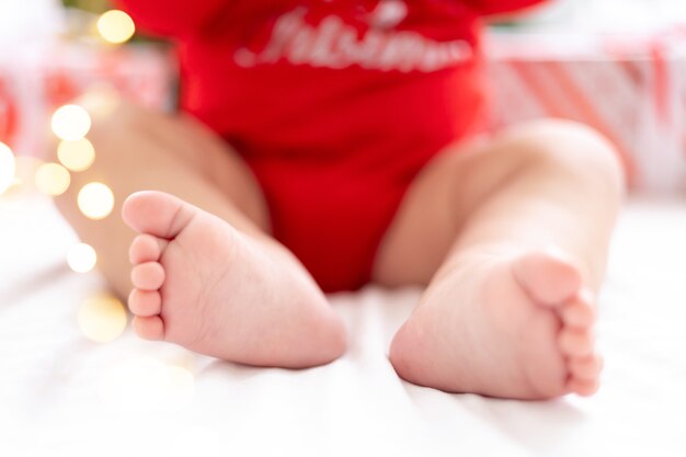 Piccole gambe di un primo piano sano del bambino sui precedenti dei regali e di un albero di natale