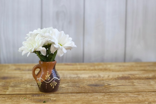 Piccole margherite bianche fresche in un vaso di argilla marrone su uno sfondo di legno chiaro primo piano