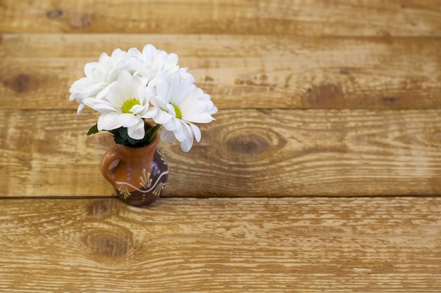 Piccole margherite bianche fresche in un vaso di argilla marrone su uno sfondo di legno chiaro primo piano